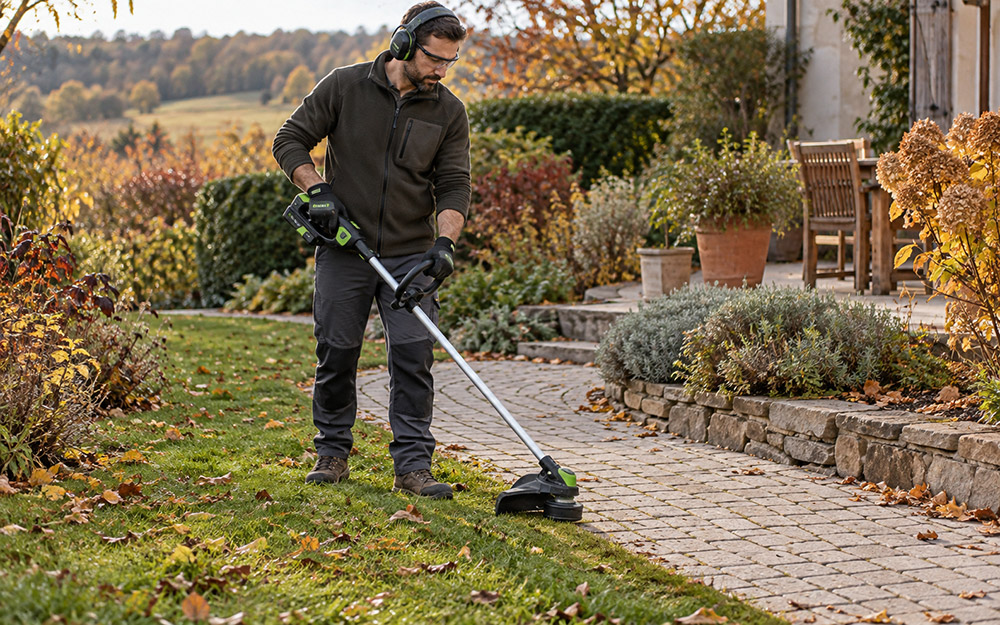 Jardinier équipé de protections réalisant les finitions d'une bordure au coupe-bordure